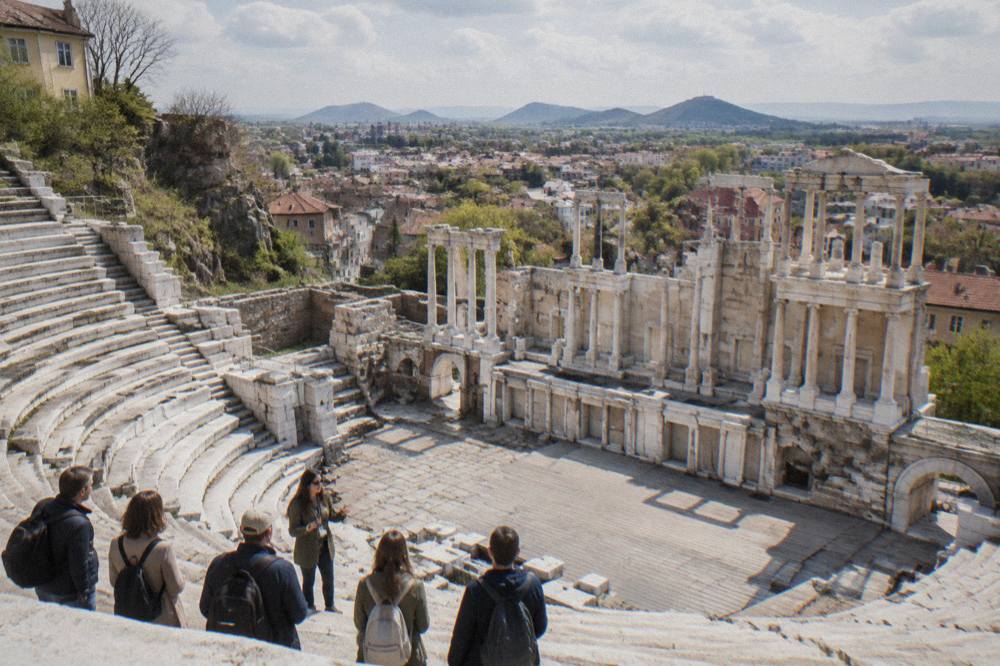 A guide speaking to a small group of travellers beside the marble rows of the Ancient Theatre of Philippopolis