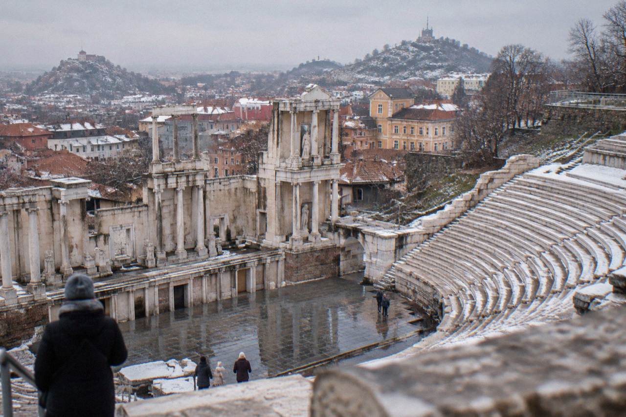 Plovdiv Old Town rooftops under a light covering of snow, with the Ancient Theatre hillside in the background