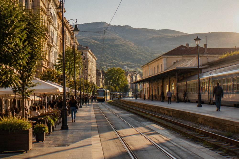 A passenger train waiting at a sunny railway platform beside a station building