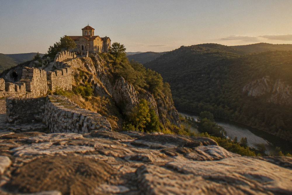 A stone fortress wall on a rocky ridge overlooking a green valley near Asenovgrad