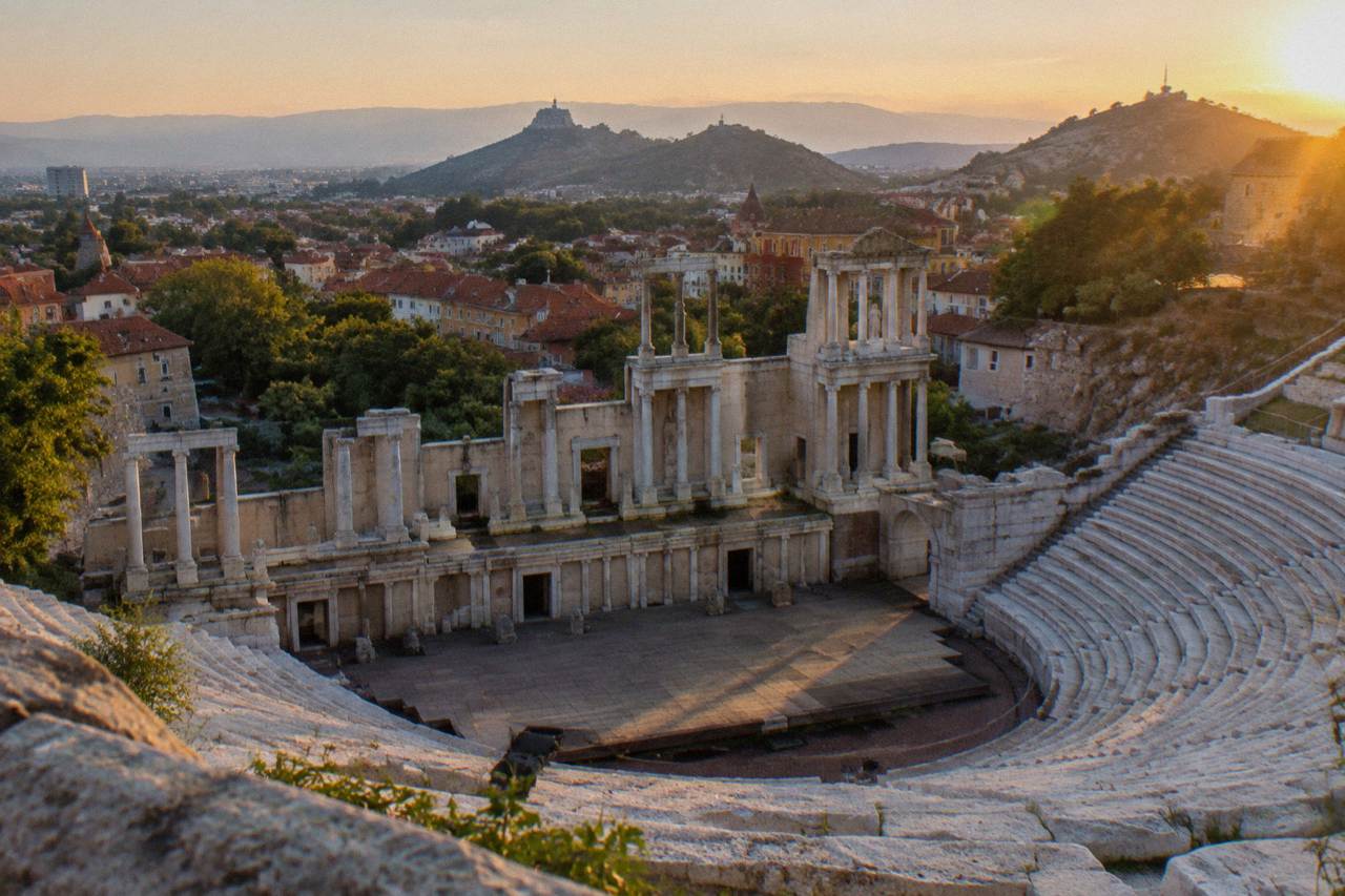 Marble rows of an ancient Roman theatre rising above red rooftops at golden hour