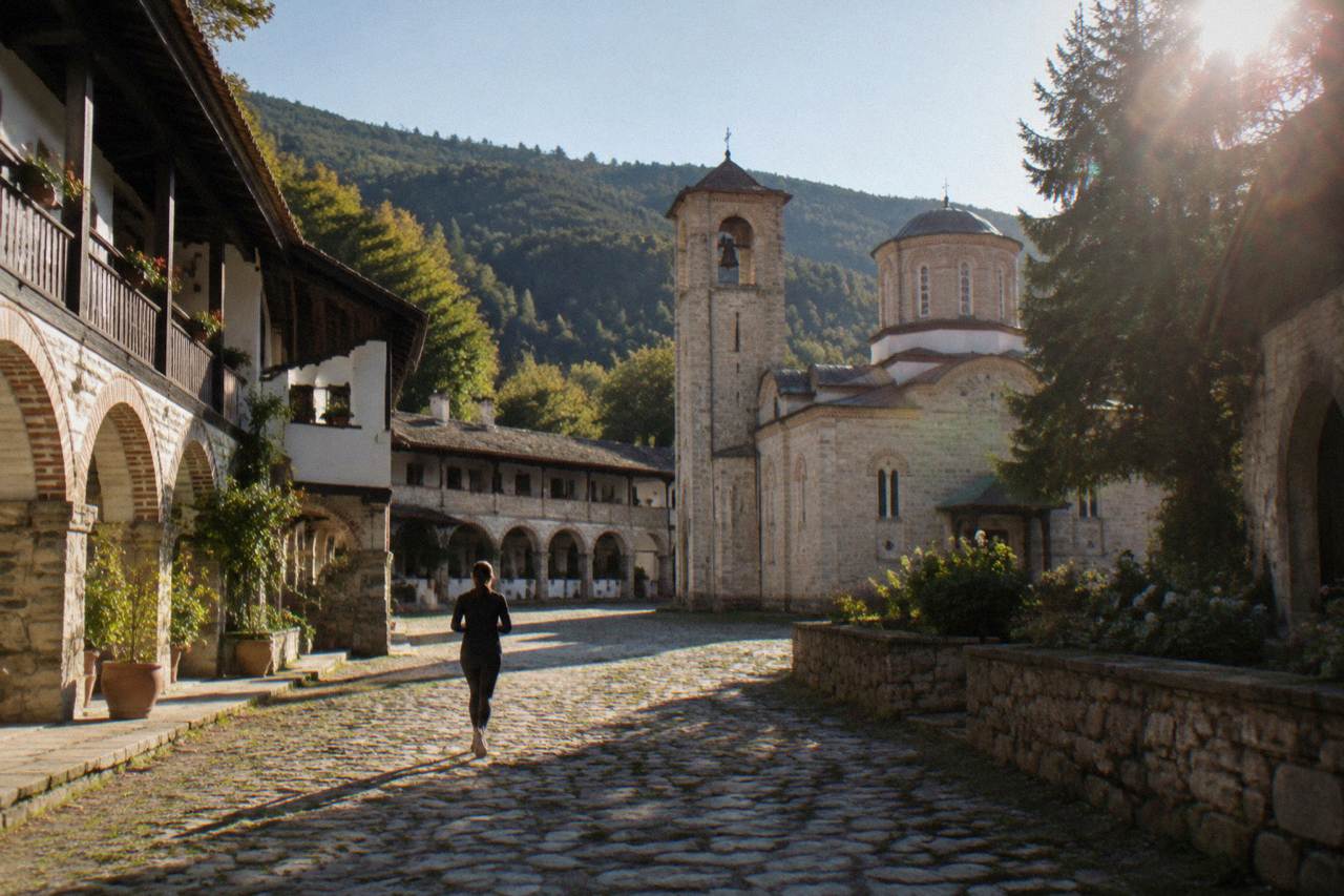 A Bulgarian monastery courtyard with stone arches and a bell tower under a clear sky