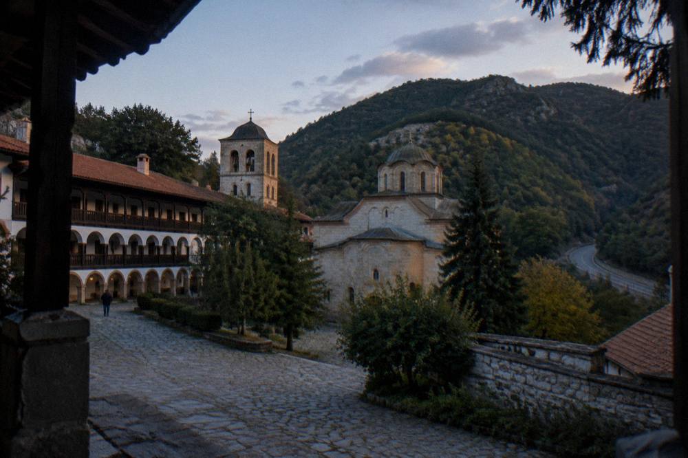 A mountain road winding through forested Rhodope hills toward a monastery