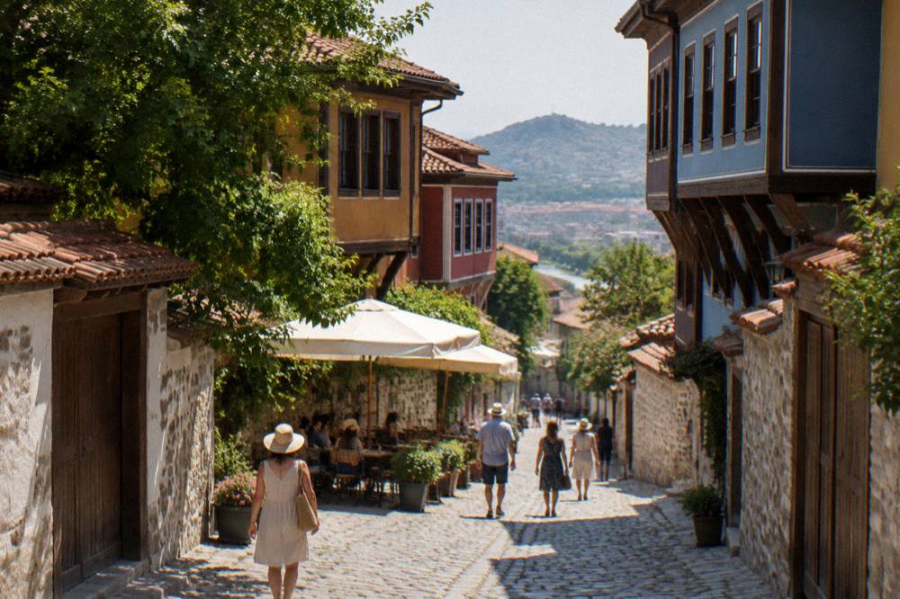 People walking a sunlit Plovdiv street in summer with parasols and cafe tables