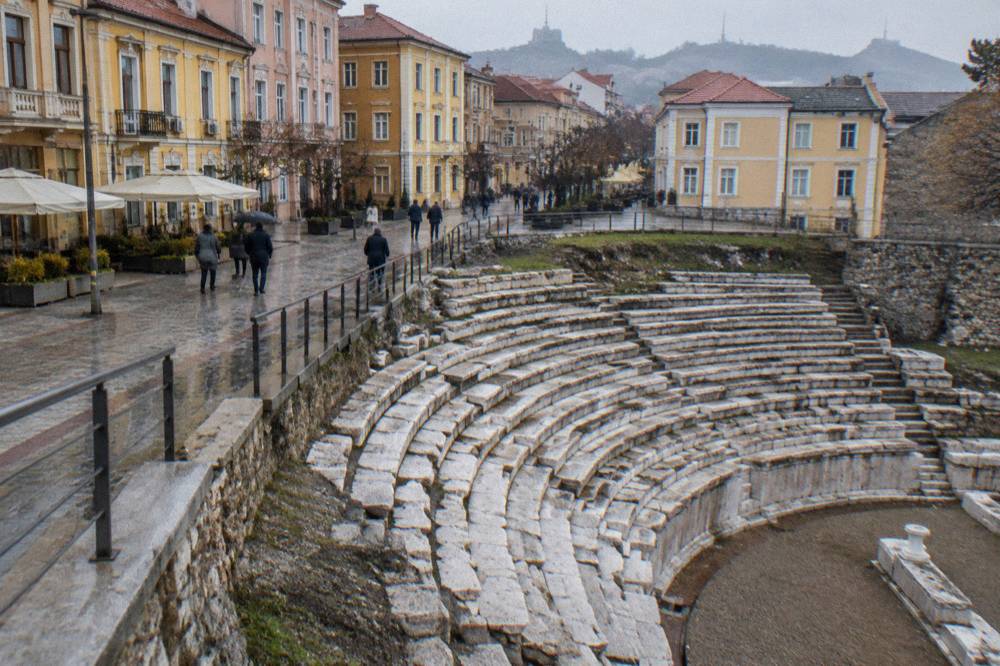 Ancient stone seating rows of a Roman stadium exposed beside a modern pedestrian street