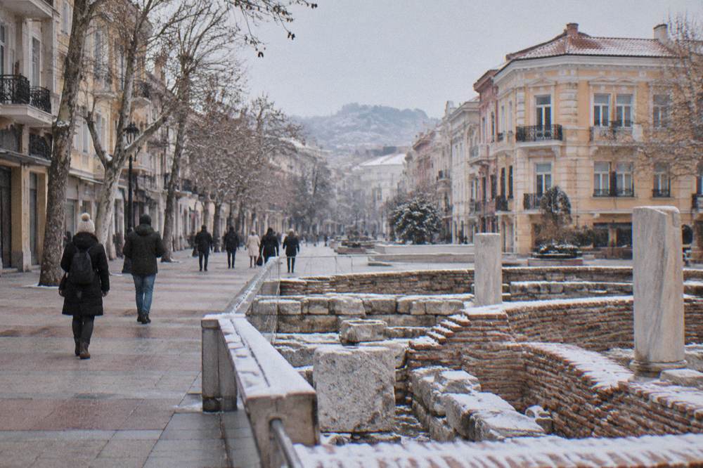 Tourists walking past excavated ancient stone ruins set into a modern city square