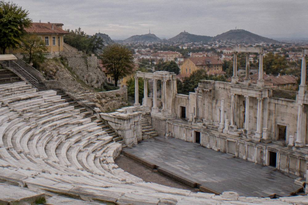 A stone stage wall with column bases facing rows of empty theatre seats