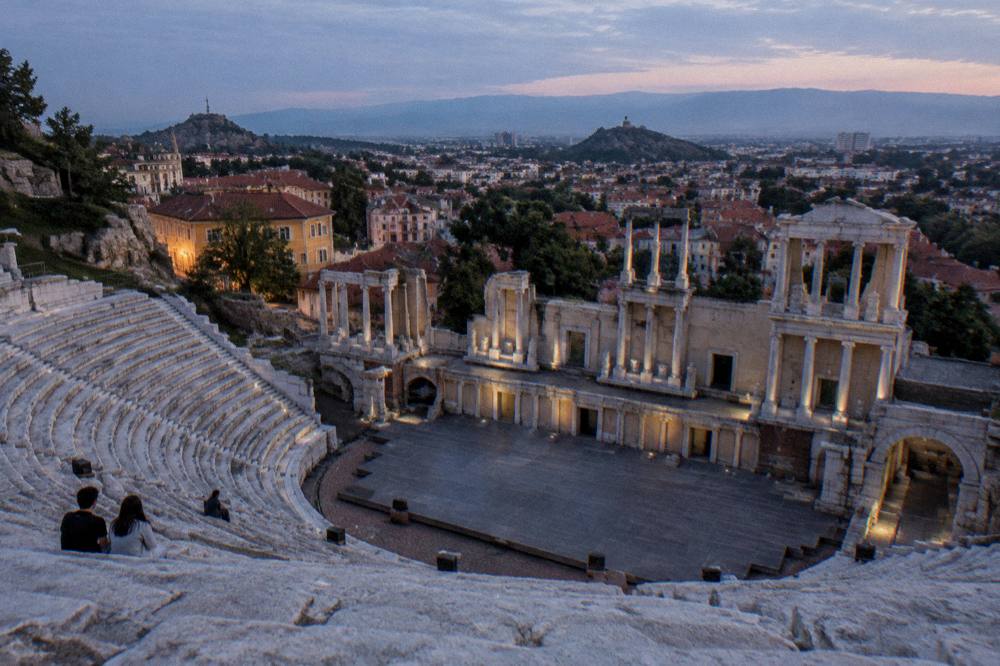 A wide view over rooftops toward distant mountains from high stone seats