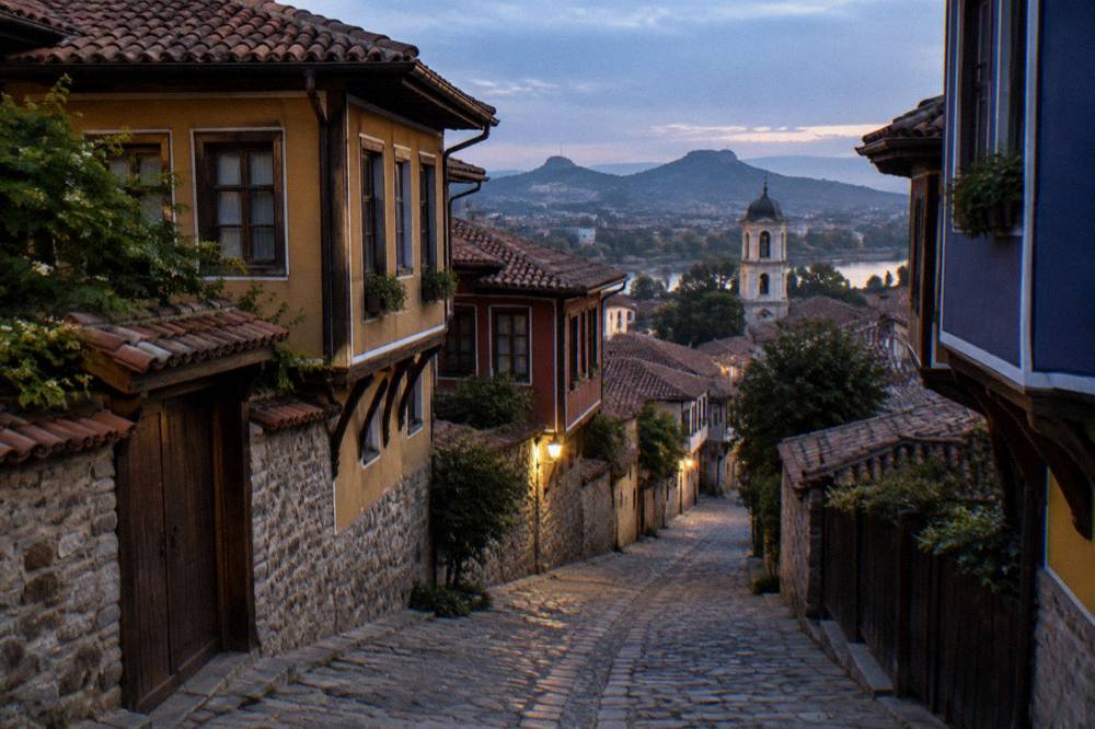 Narrow cobblestone street in central Plovdiv with old houses and a church tower in the distance