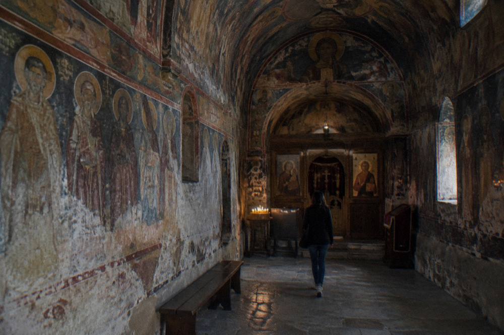 Painted frescoes covering the walls and ceiling of a small Orthodox church interior