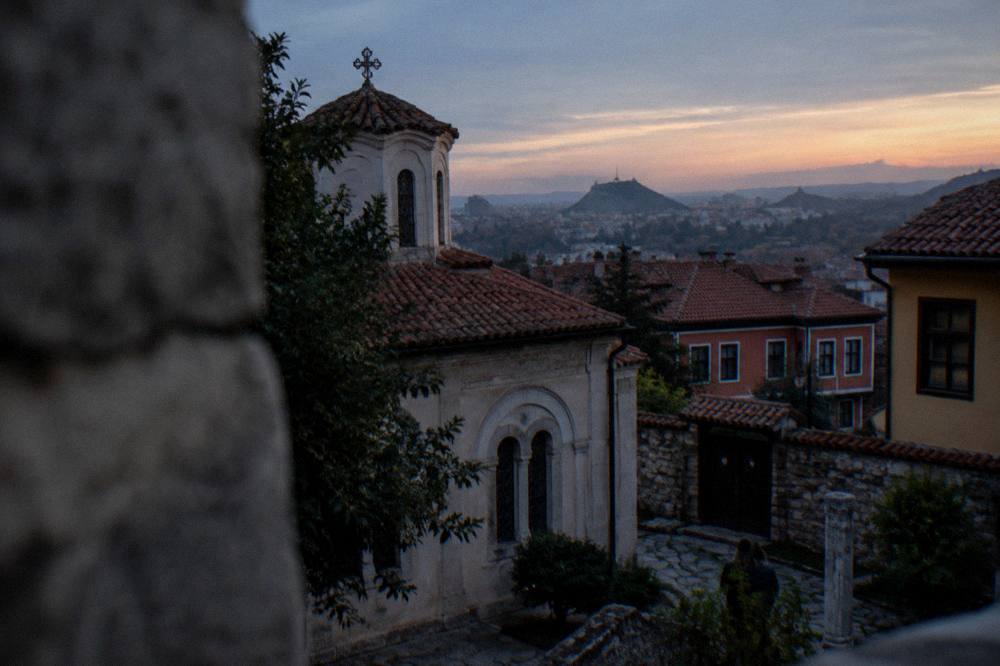 A hilltop viewpoint over red rooftops and distant hills at sunset