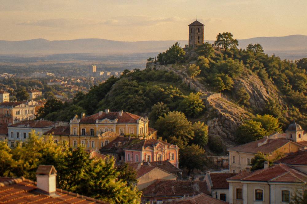 A stone clock tower on a small wooded hill above a Balkan old town
