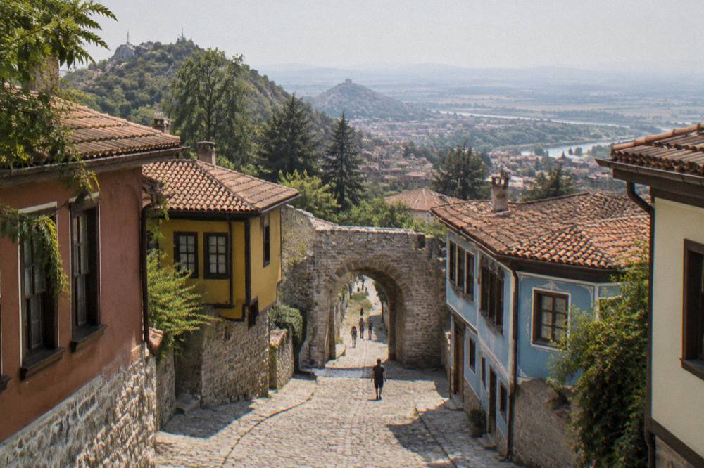 A narrow cobbled street in an old Balkan town with colourful houses and a stone gate ahead