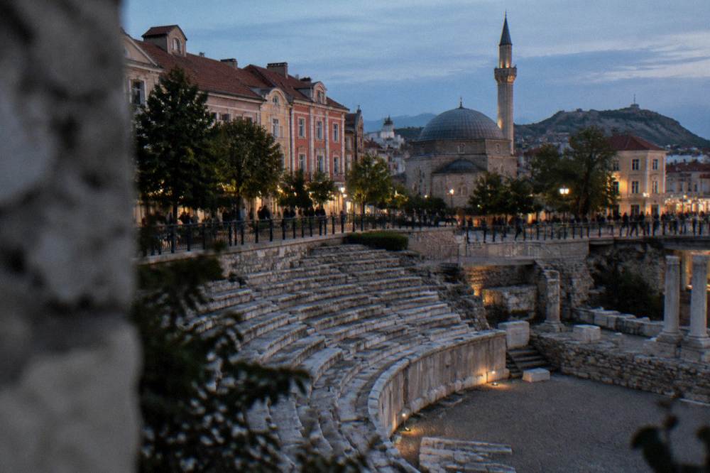 Grey-domed mosque beside a pedestrian street with ancient stadium remains