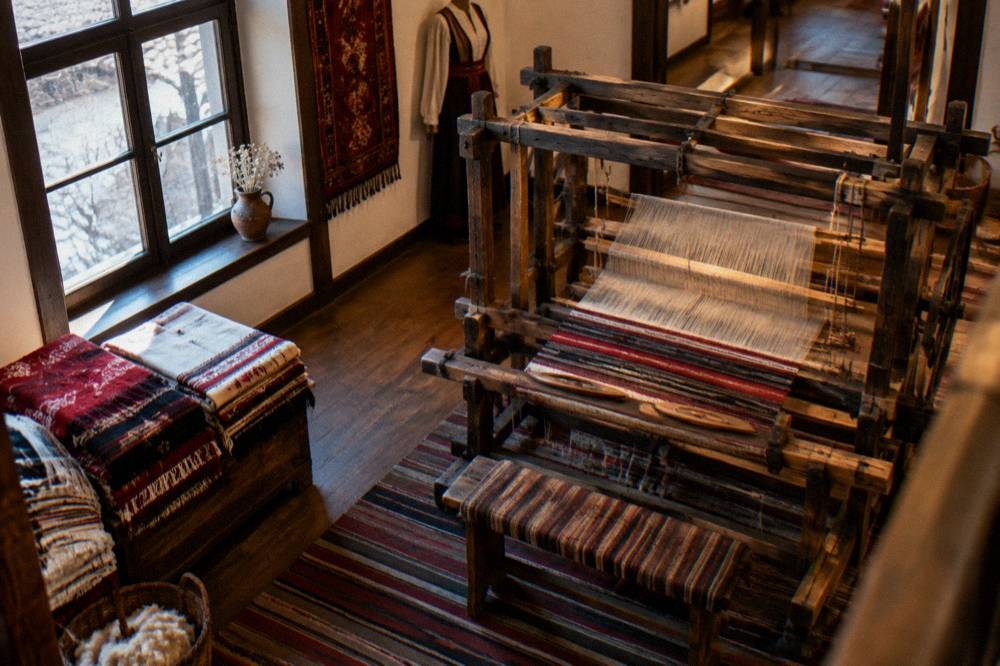 A museum interior with a traditional Bulgarian loom and folded woven textiles under warm light
