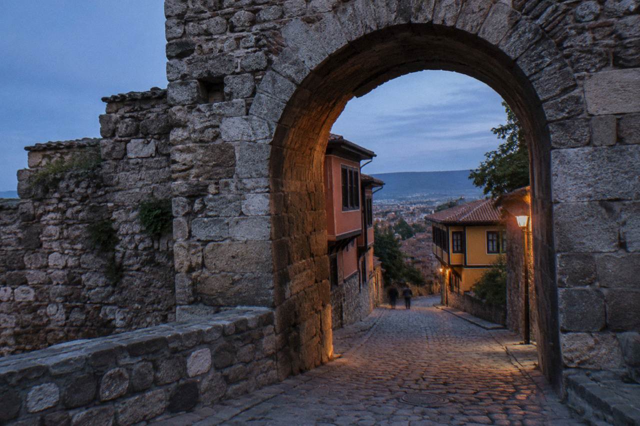 The stone arch of Hisar Kapia, an old gate in Plovdiv, with cobbled street and colourful houses beyond