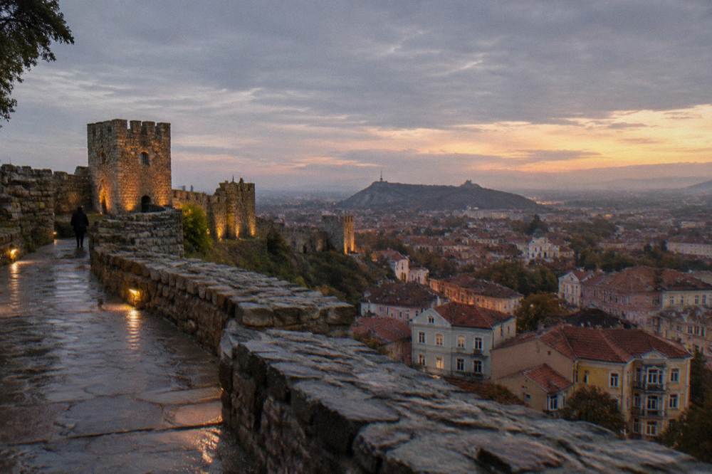 Restored hilltop fortress walls at dusk above city rooftops