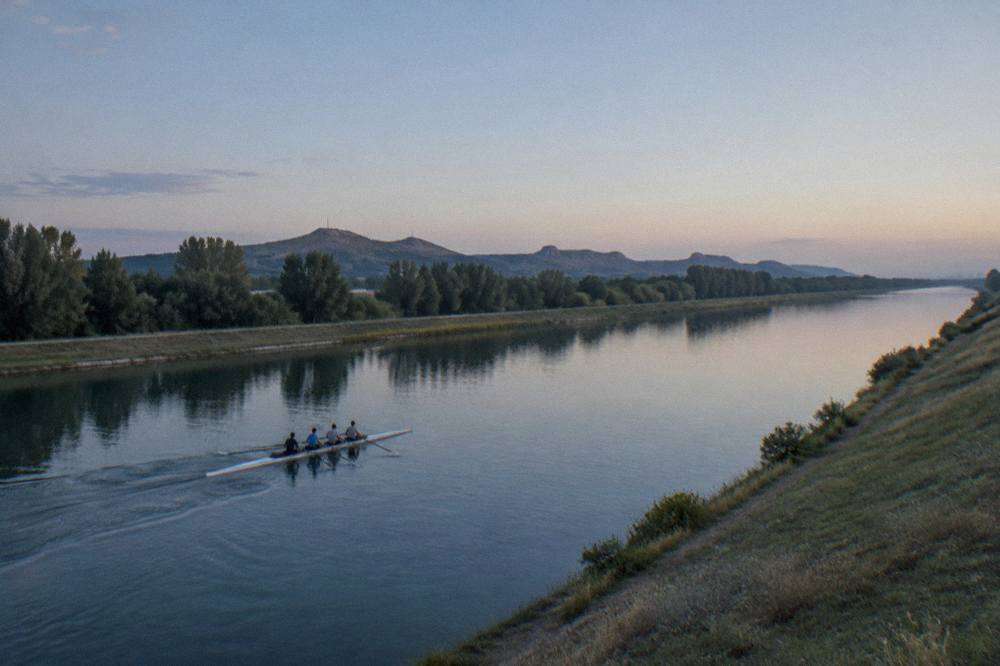 Rowers in a narrow shell cutting across the flat water of the canal in early morning light
