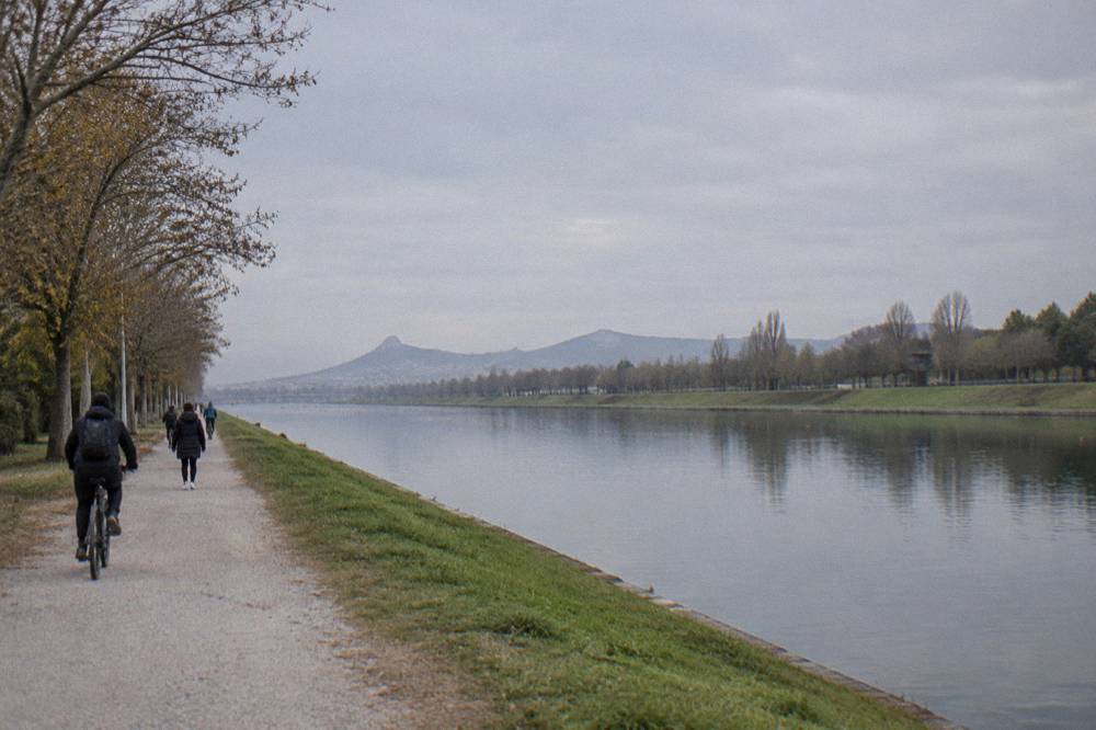 Cyclists and walkers on a flat gravel path beside the water with trees along the bank