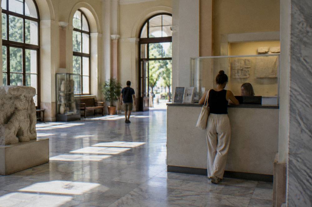 A museum ticket desk with a visitor speaking to staff in a bright lobby