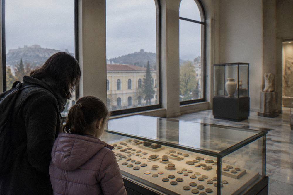 A child and an adult examining a museum case of ancient coins