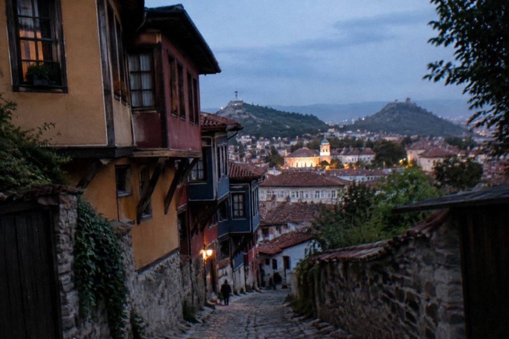Evening view over Plovdiv rooftops with illuminated historic buildings and hills beyond