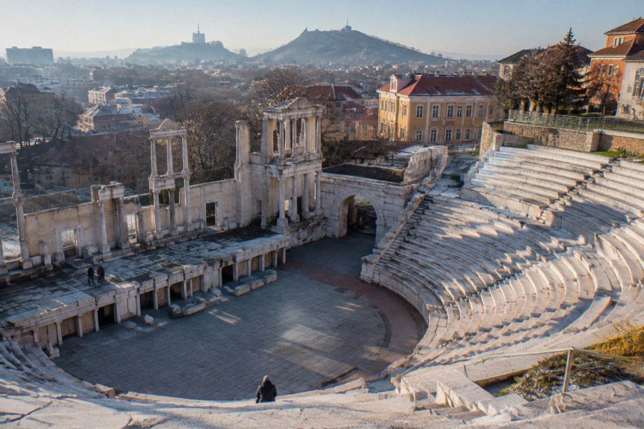 A small semicircular Roman stone theatre with stepped marble seating rows rising around a flat orchestra floor