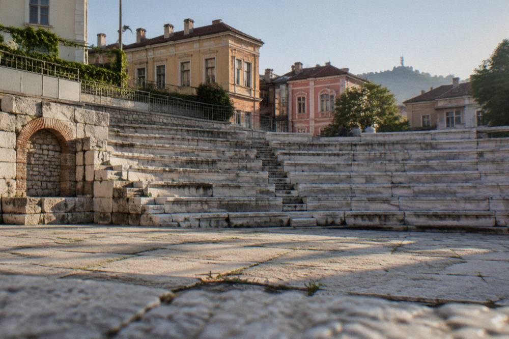 The curved stone seating of a small Roman odeon seen from the orchestra floor, with the walls of later buildings behind it