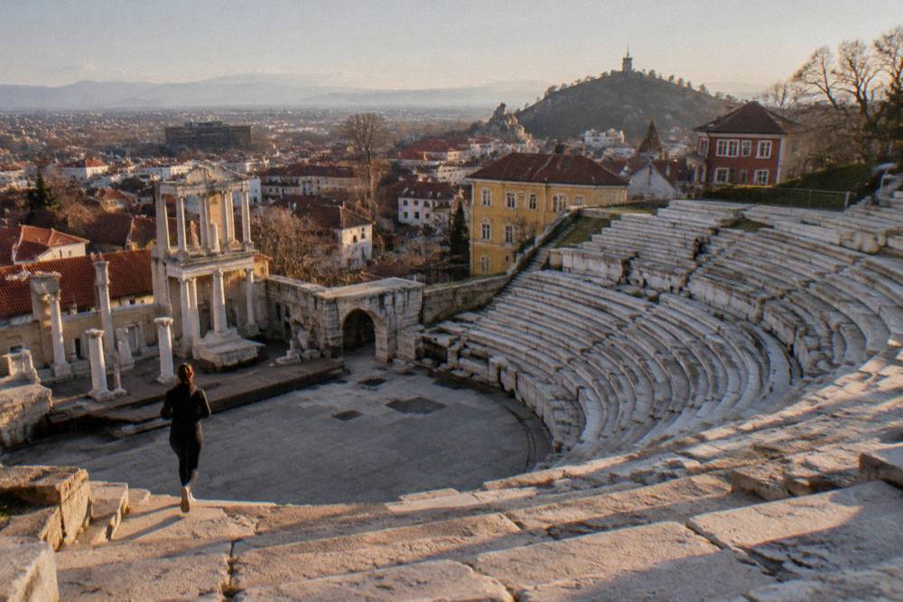 Golden late afternoon light falling across ancient stone ruins on a hillside above red rooftops