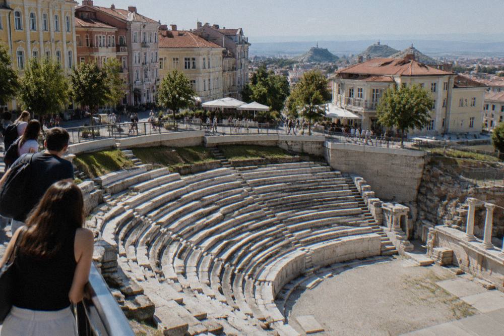 Visitors looking down at the exposed stone rows of the Roman Stadium from Dzhumaya Square in Plovdiv