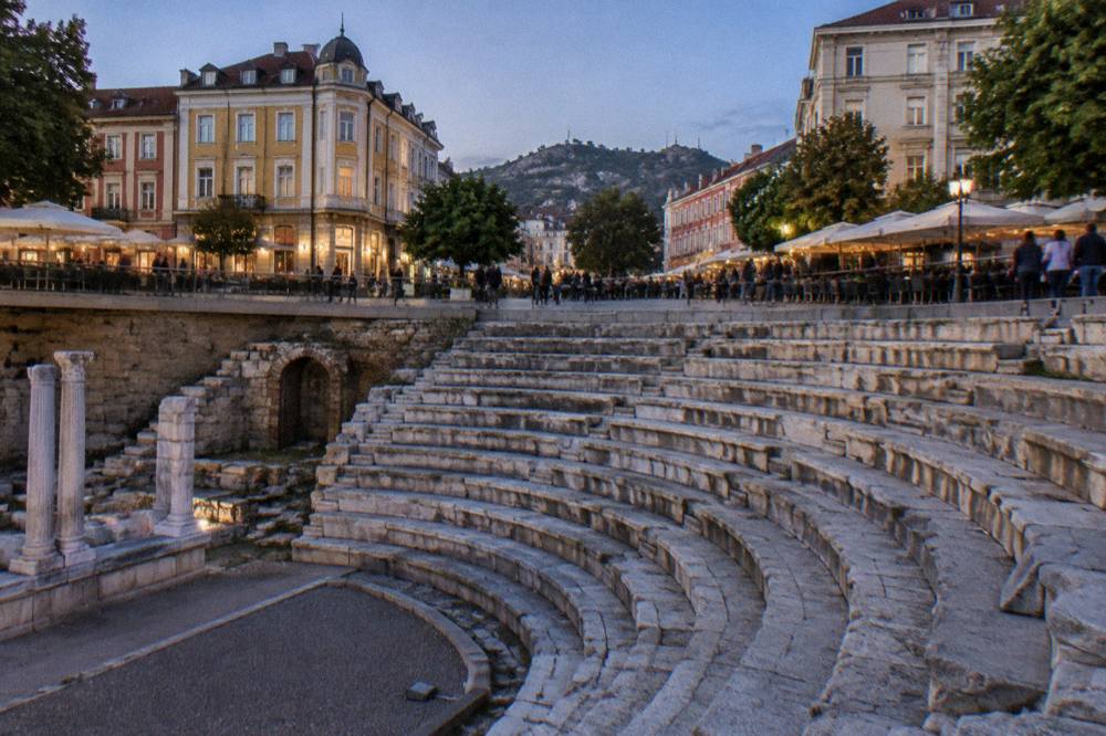 Cafe tables and pedestrians filling Dzhumaya Square around the sunken Roman Stadium remains in Plovdiv