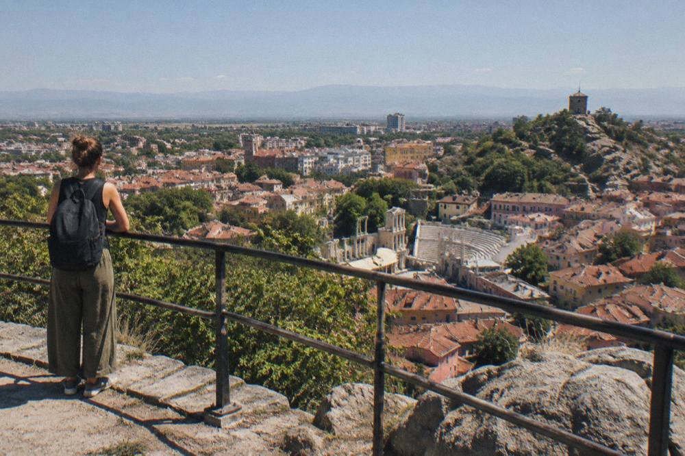 A traveller standing at a hilltop railing looking out over a city panorama