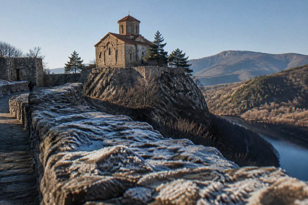 A small stone church with a steep tile roof standing inside fortress walls on a hilltop