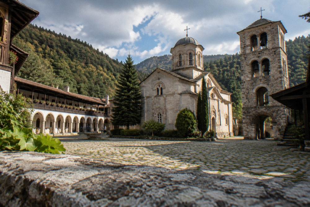 Hillside Orthodox monastery with arcaded courtyard and bell tower in a wooded valley