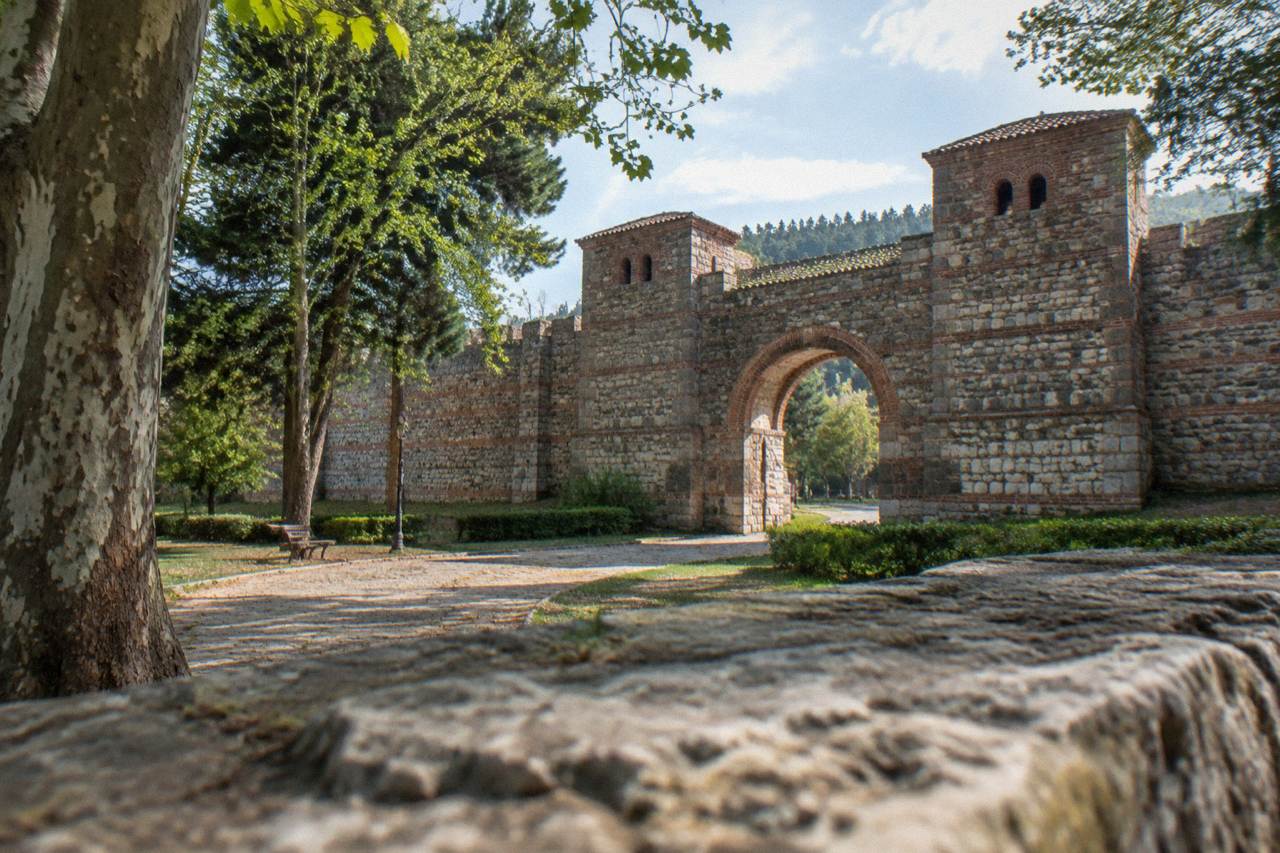 Stone Roman fortress wall with an arched gate standing above a quiet park