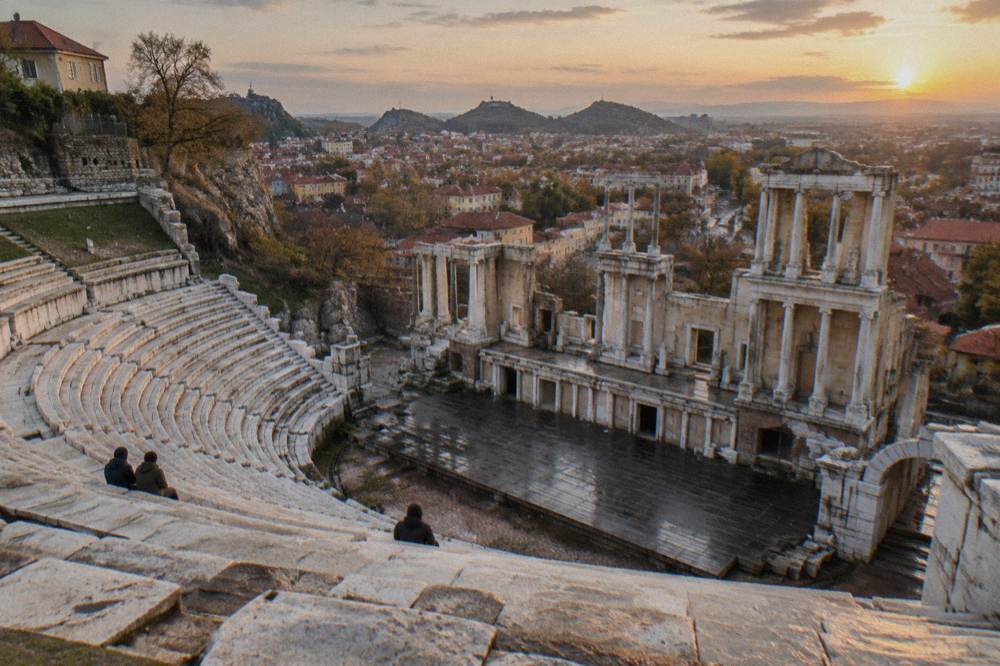 Marble rows of an ancient theatre rising against a city skyline at golden hour