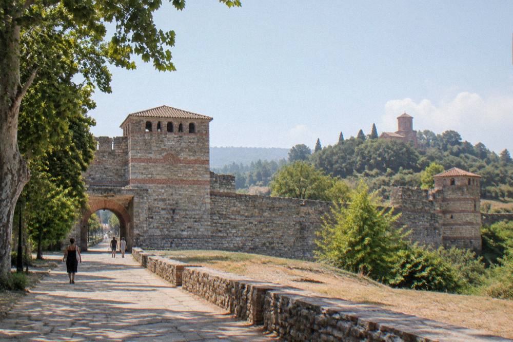 A red monastery church tower behind stone walls on a green hillside