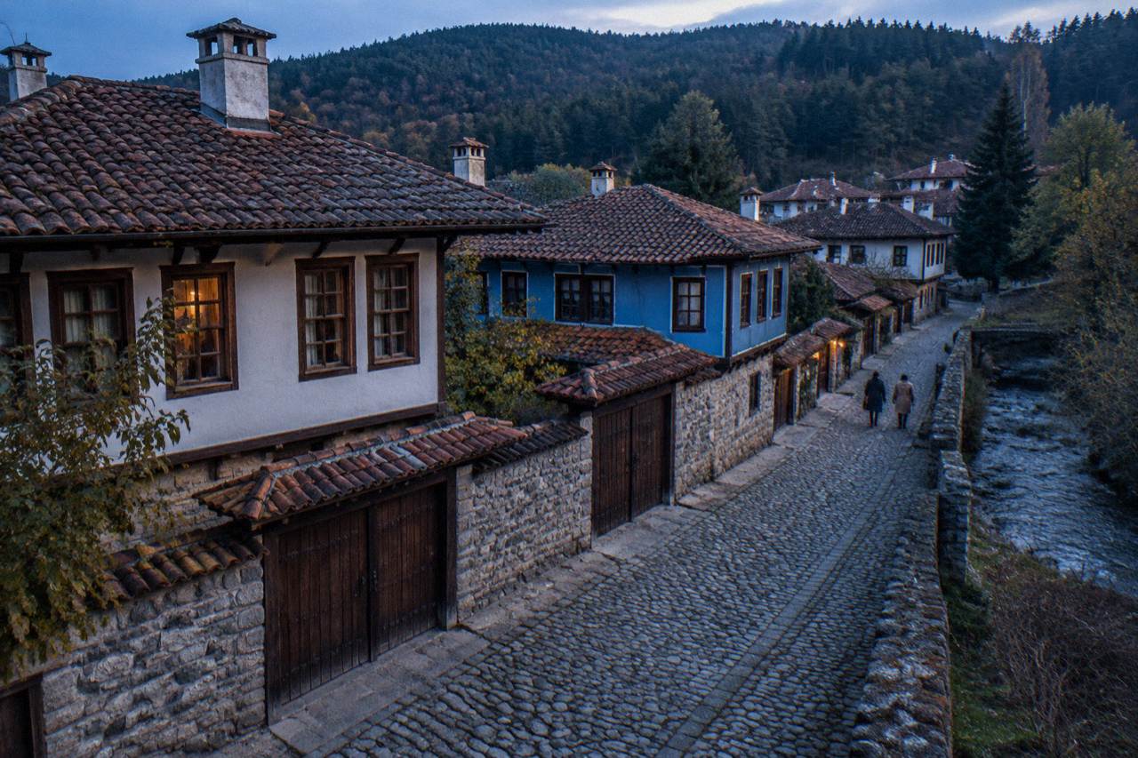 Cobbled street lined with low stone walls and restored revival-era houses in a mountain town