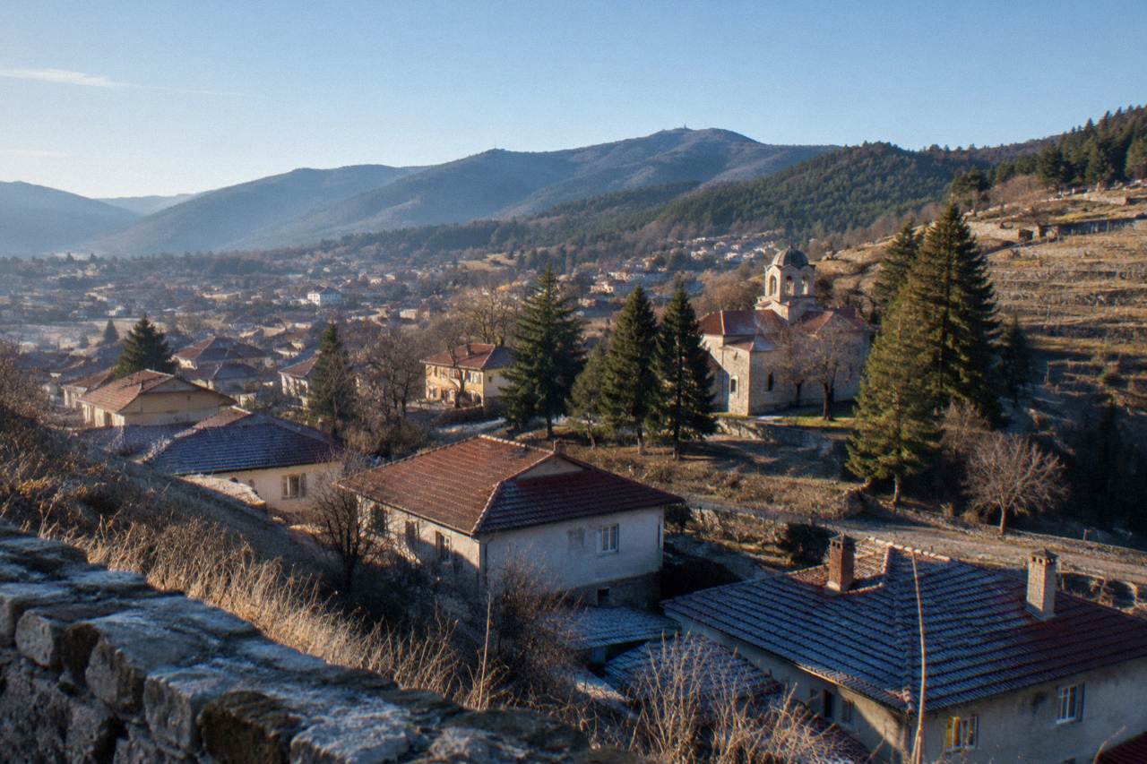 A small Bulgarian town of red rooftops and church domes set among green hills on a clear day