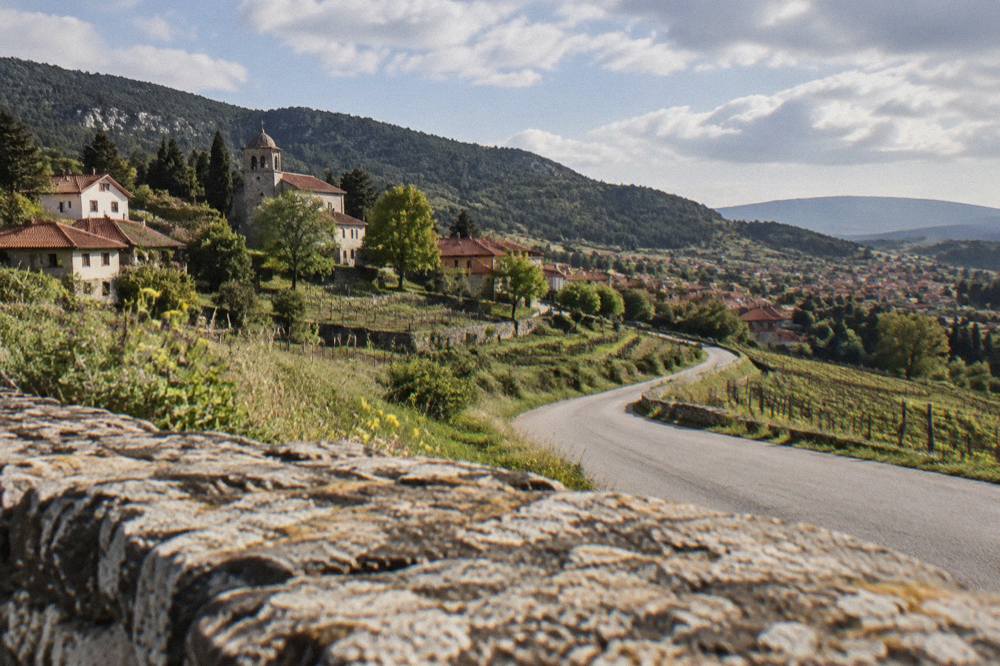 A country road winding through vineyards and low hills toward a small town in the distance