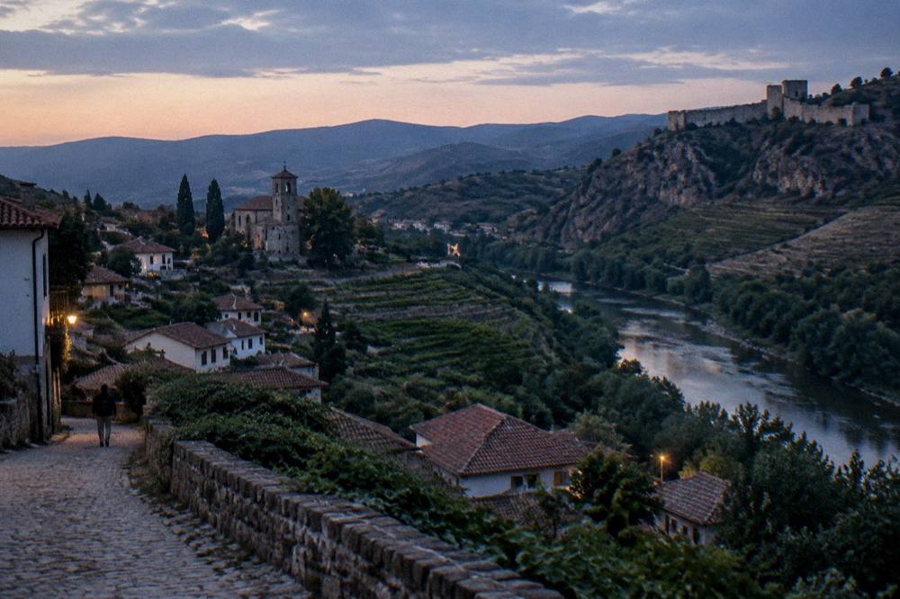 A medieval fortress wall on a rocky ridge above a river valley in the Rhodope foothills