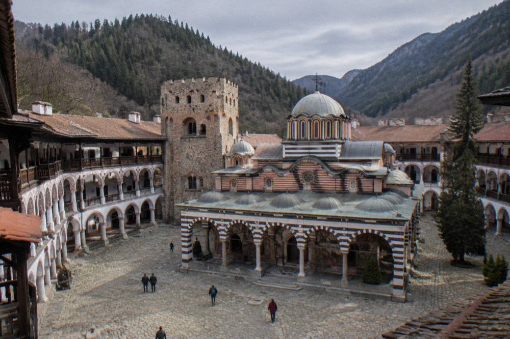 Monastery courtyard with arched stone galleries on three sides and a church tower