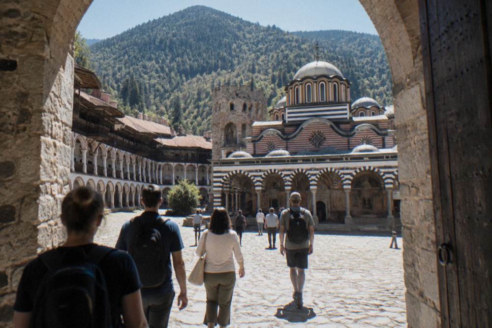 Group of visitors walking through a stone monastery gate into a courtyard