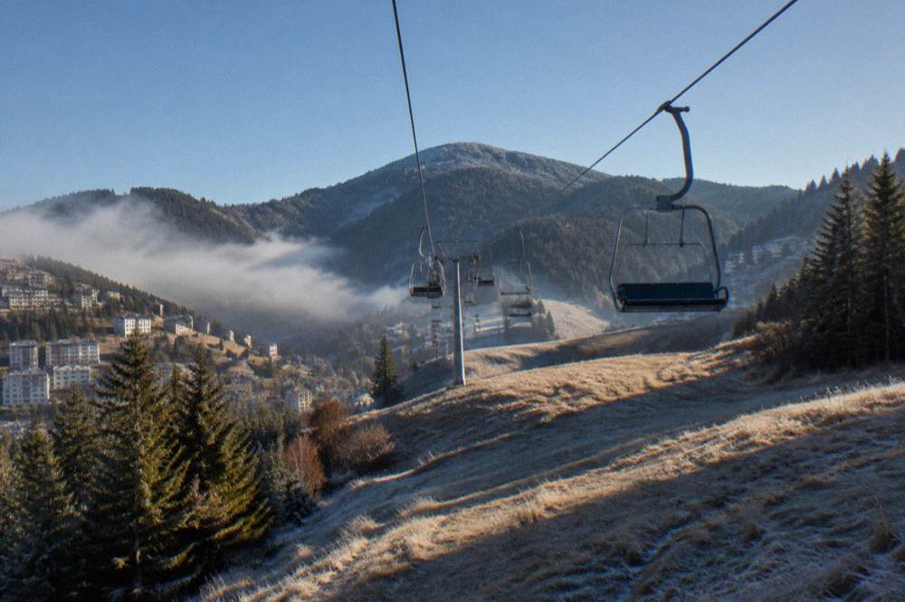A ski lift line rising over grassy slopes toward a rounded mountain peak