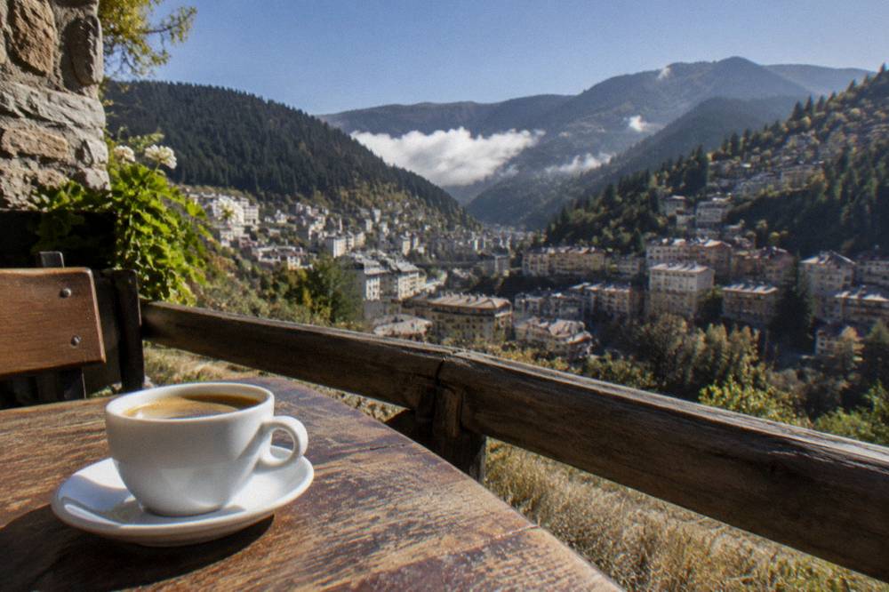 A cup of coffee on a wooden table beside a mountain view