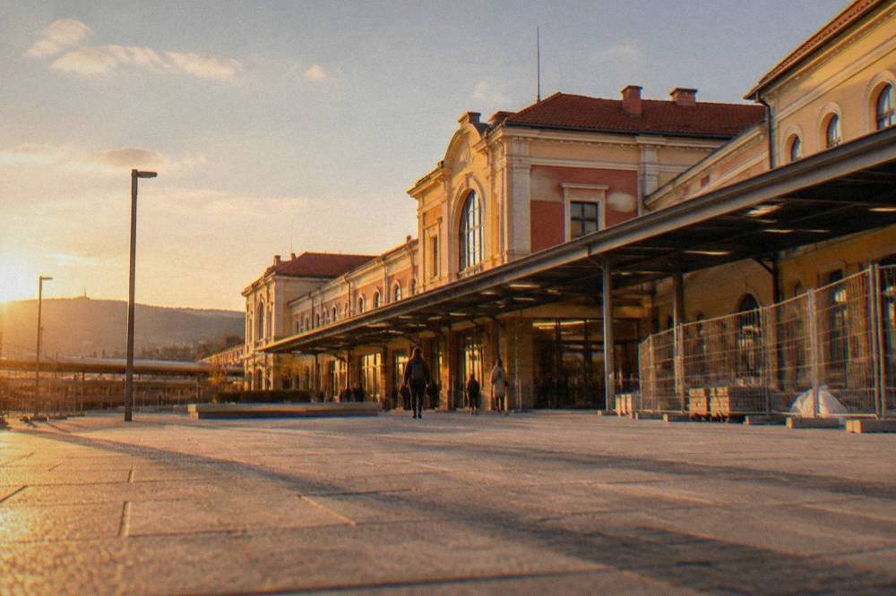 A modern Bulgarian railway station concourse with departure boards and travellers with luggage