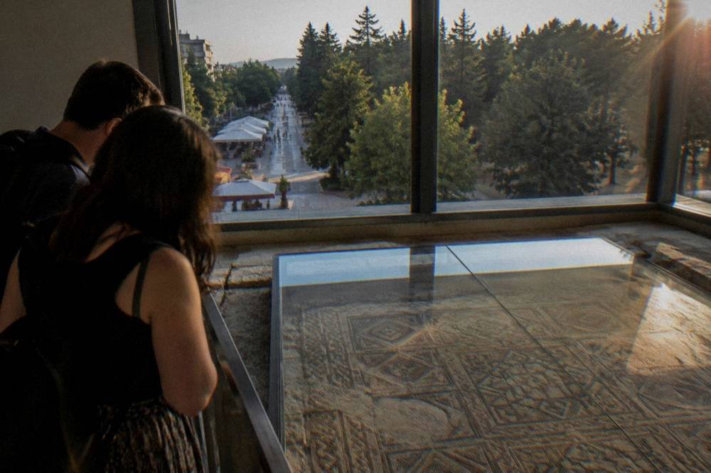 Two people looking at glass-covered ancient floor mosaics in a museum