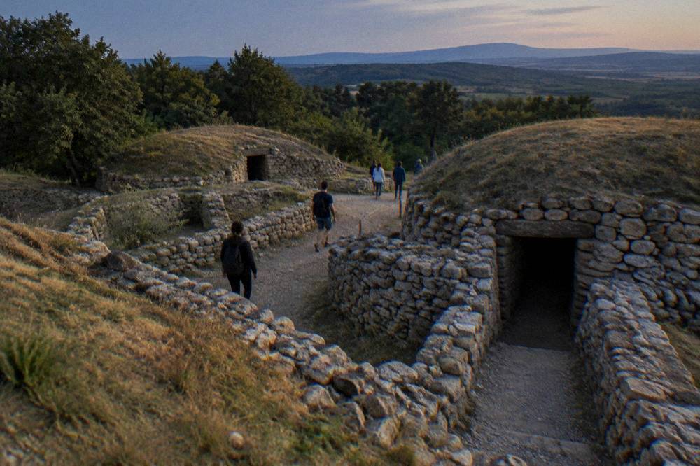 Visitors walking a path between stone walls at a hilltop archaeological site
