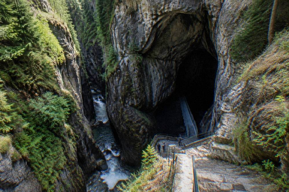 A huge dark cave opening in a rock face with a metal staircase leading down into it