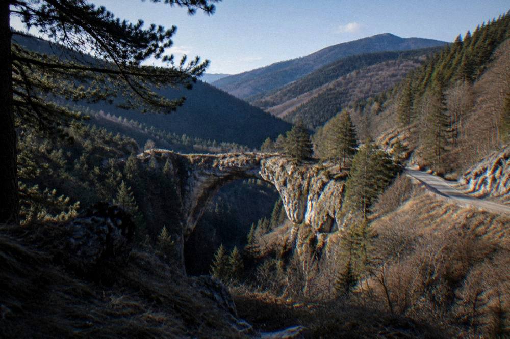 A stone arch bridge of rock spanning a forested valley in the Rhodope Mountains